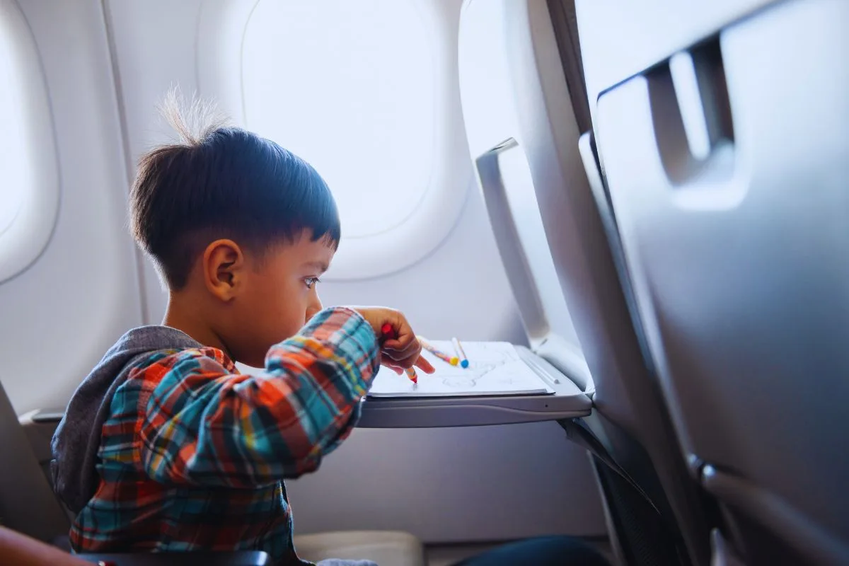 Endormir les enfants durant un vol : Un jeune garçon se concentre sur son dessin à bord d'un avion.