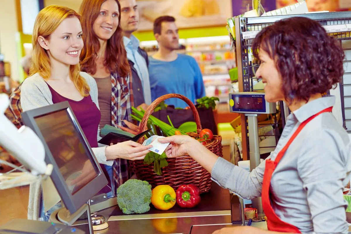 Cliente heureuse payant ses courses à la caisse d'un supermarché avec d'autres clients en attente.